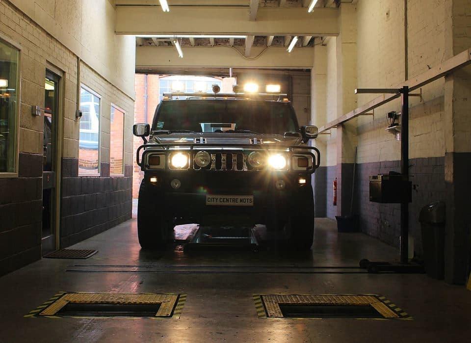 A vehicle head-on in the MOT test lane at City Centre MOTs, headlamps blazing over the lift plates